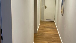 Valkoisilla seinillä ja puulattialla varustettu käytävä, joka johtaa käytävän päässä olevaan oveen.