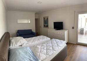 Ett sovrum med en säng, en byrå, en tv och en dörr som leder ut till en balkong.