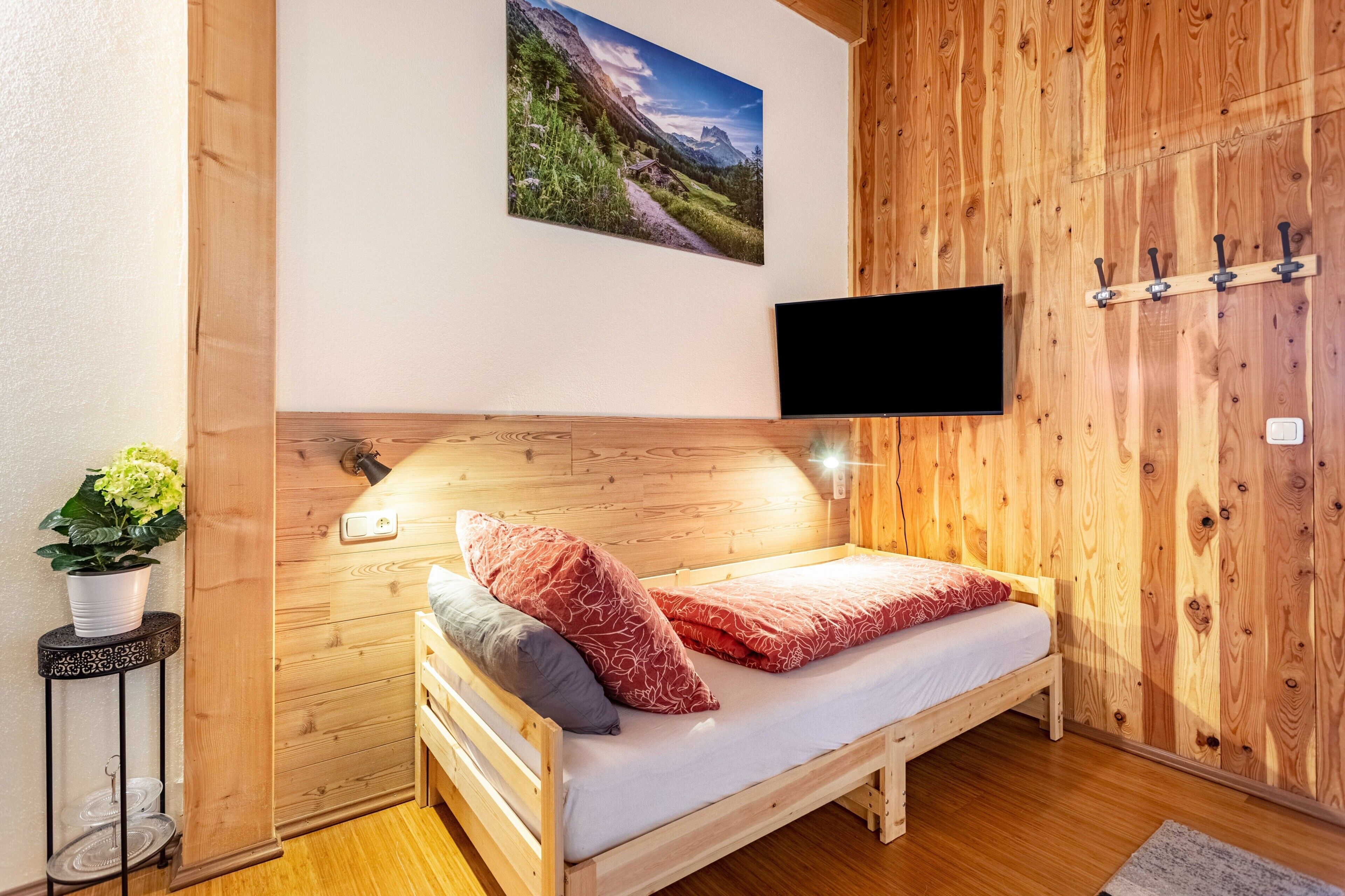 Cama de madeira com uma televisão montada, um vaso de planta e uma parede de madeira com um quadro.