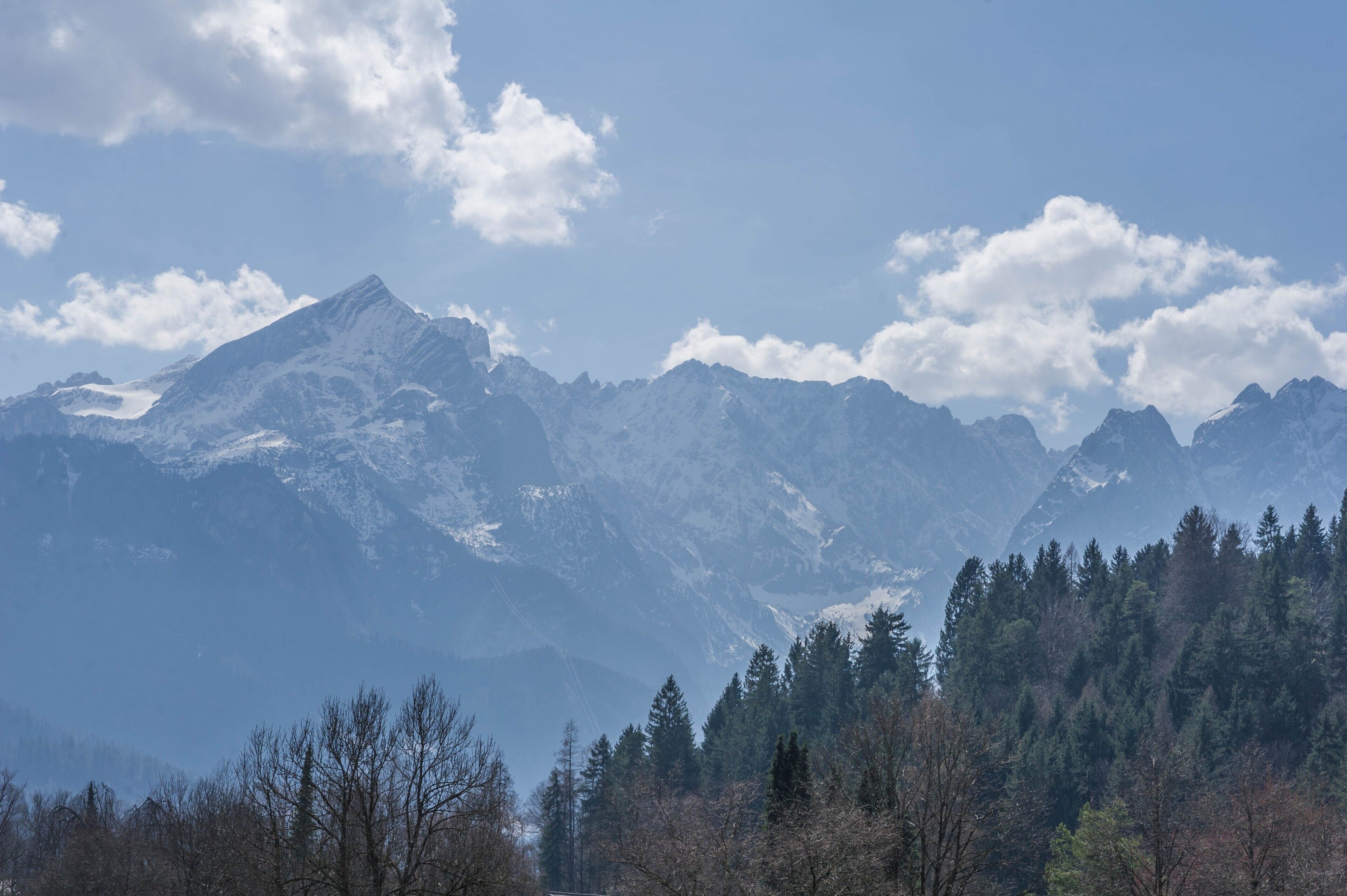 A mountain range with snow-capped peaks and a forested foreground.