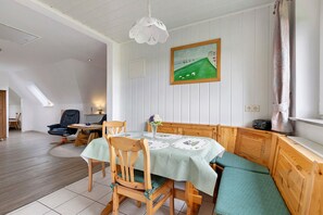 A dining area with a table set for four, wooden chairs, a bench, a painting on the wall, and a ceiling light.