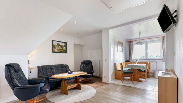 Un salon moderne comprenant un canapé, des fauteuils, une table  à manger et un téléviseur fixé au mur.