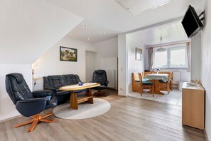 A modern living room with a sofa, chairs, a dining table, and a TV mounted on the wall. - Apartment 'I Raup' with Shared Garden, Balcony and Wi-Fi (Winnert)