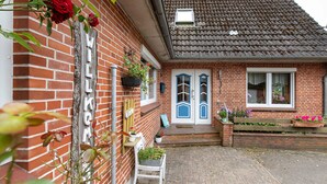 Une maison en briques avec une pancarte indiquant « BIENVENUE », une chaise blanche et un petit jardin.