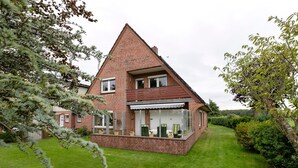 Une maison à deux étages, avec une façade en briques, un balcon et une pelouse bien entretenue.