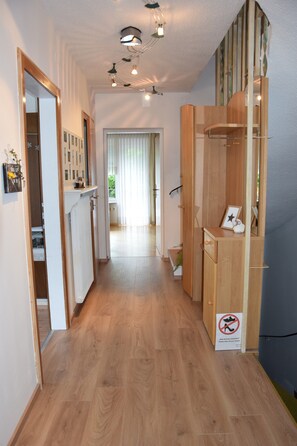 A hallway with wooden flooring, a mirror, a wooden cabinet, and a door leading to another room.