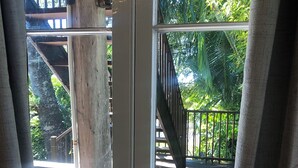Blick durch ein Fenster auf eine Holzterrasse und eine Treppe, die in einen begrünten Außenbereich führt.