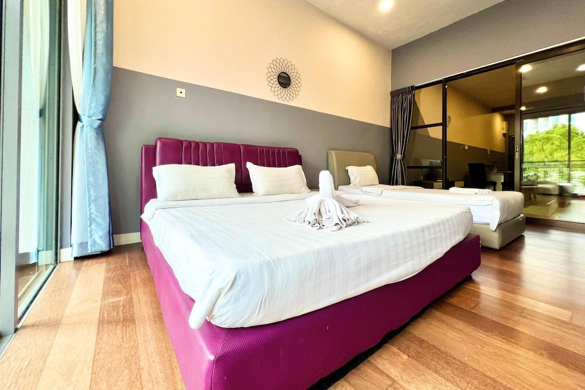 A modern hotel room with a large bed, a separate seating area, and a view through a glass door.