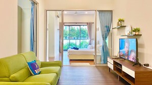 A modern hotel room with a green sofa, a TV, a wooden desk, and a balcony with a bed.
