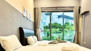 A hotel room with a large bed, a headboard, a window with curtains, and a view of buildings and trees outside.
