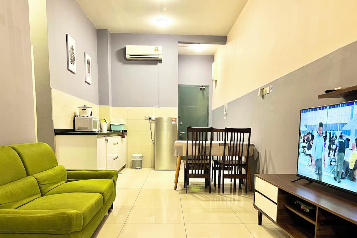 A modern living room with a green sofa, a dining table with chairs, a TV, and a kitchen area with appliances.