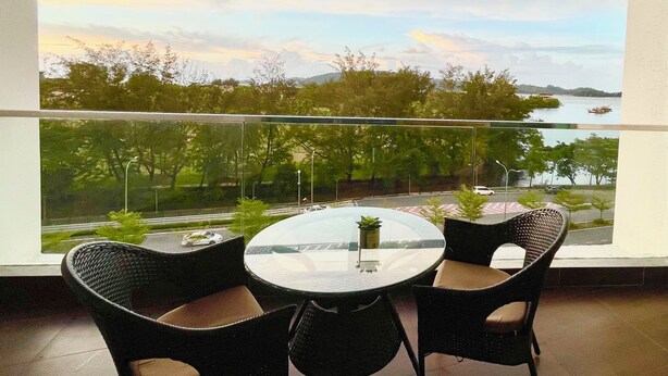 A balcony with a round table and two chairs, overlooking a body of water and greenery.