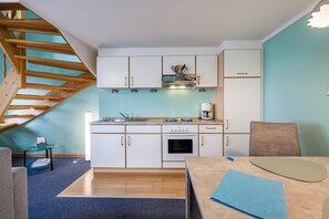 Una cocina compacta con armarios blancos, una escalera de madera y un comedor con una mesa y sillas.
