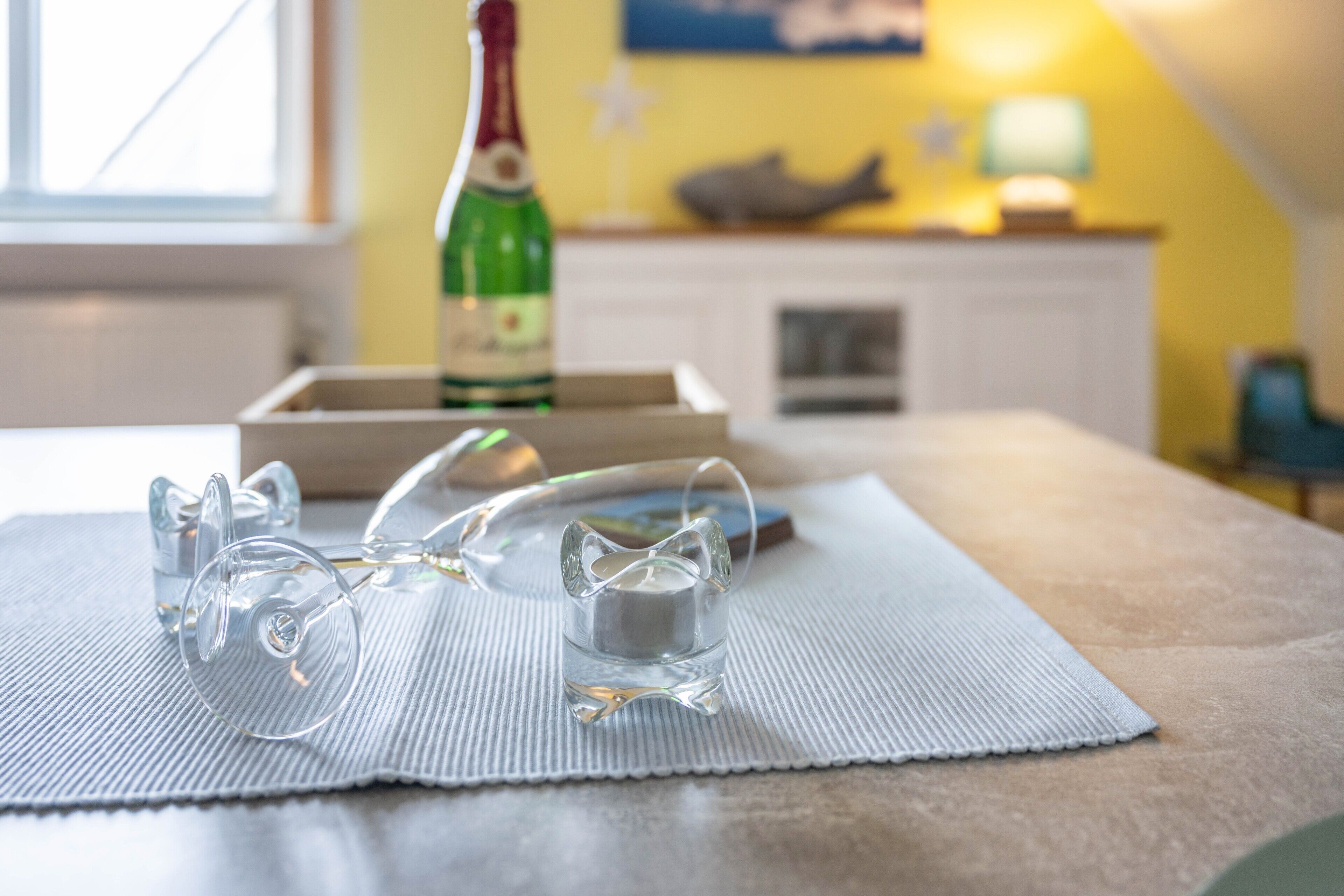 Een helder glazen glas op een geribbelde mat, een fles champagne en een houten doosje op een tafel.