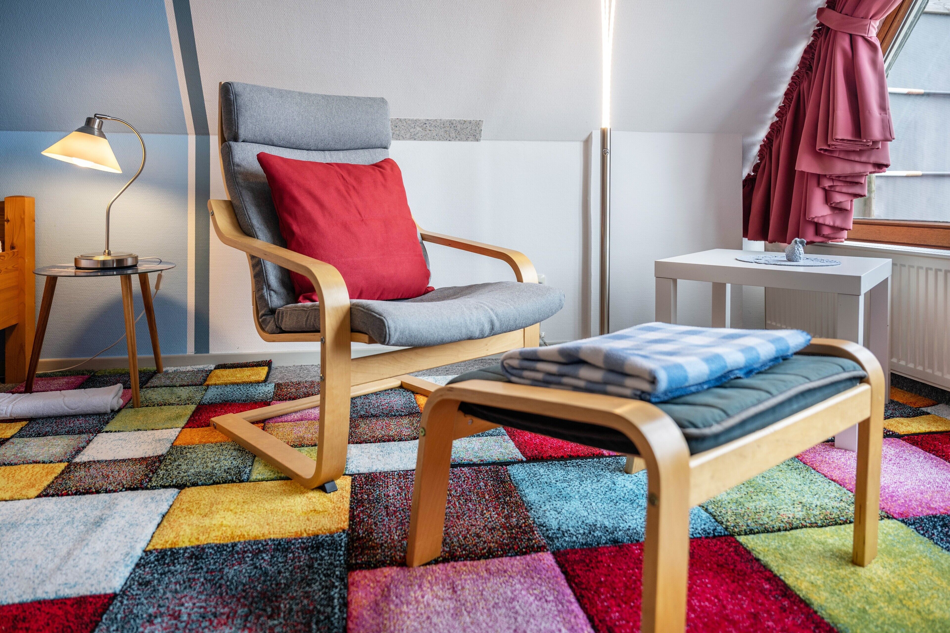 Une pièce avec une chaise en bois, une petite table, un tapis coloré et une lampe.