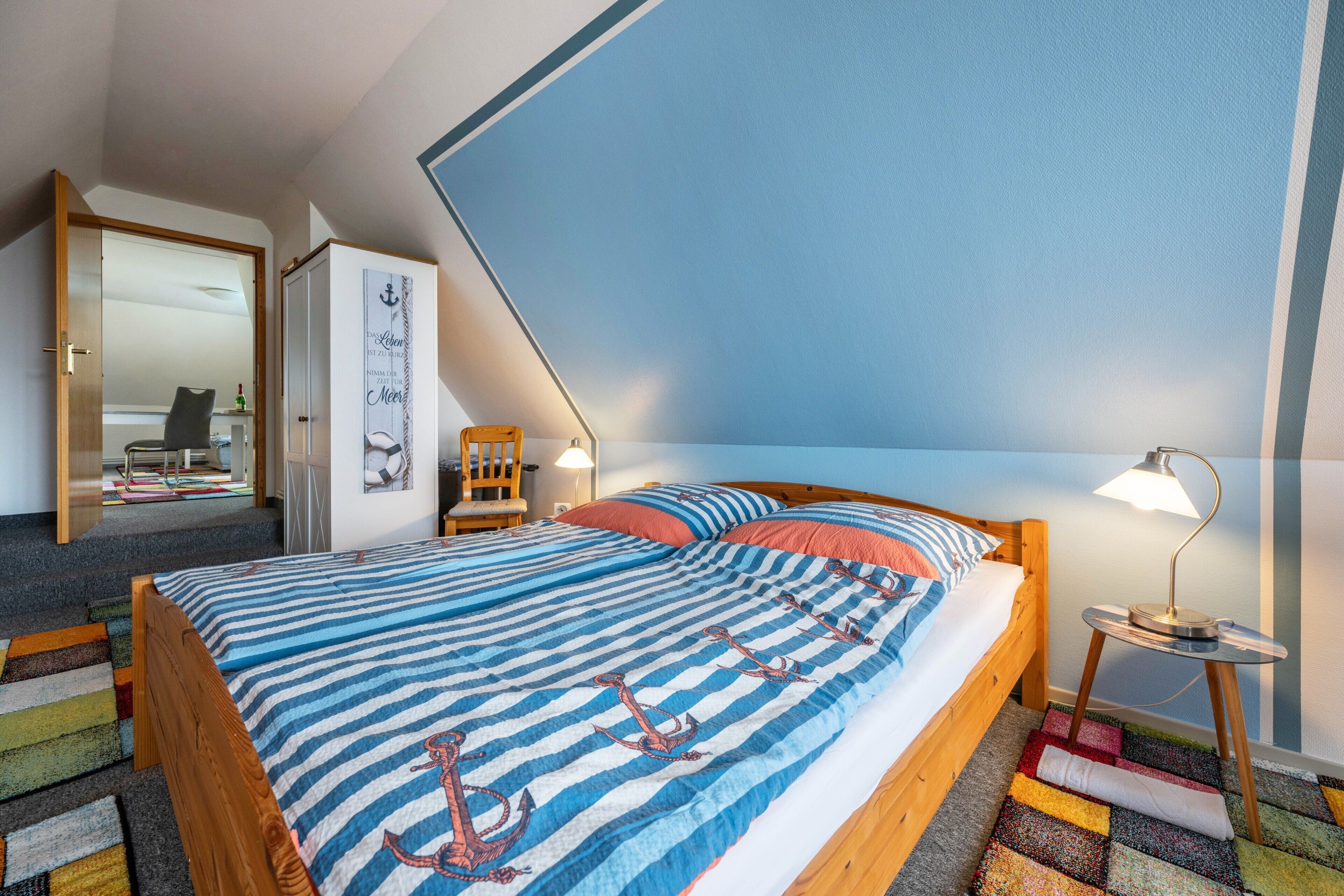 A bedroom with a bed, a nightstand, a chair, a lamp, a mirror, and a door.
