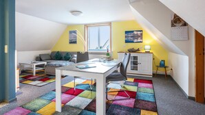 A cozy room with a white table, a sofa, a colorful rug, and a window with a view. - Apartment 'Bi Buje' with Balcony and Wi-Fi (Nordstrand)