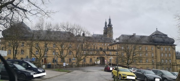 A historic building with a prominent tower, a parking lot with cars, and a sign indicating a parking zone.