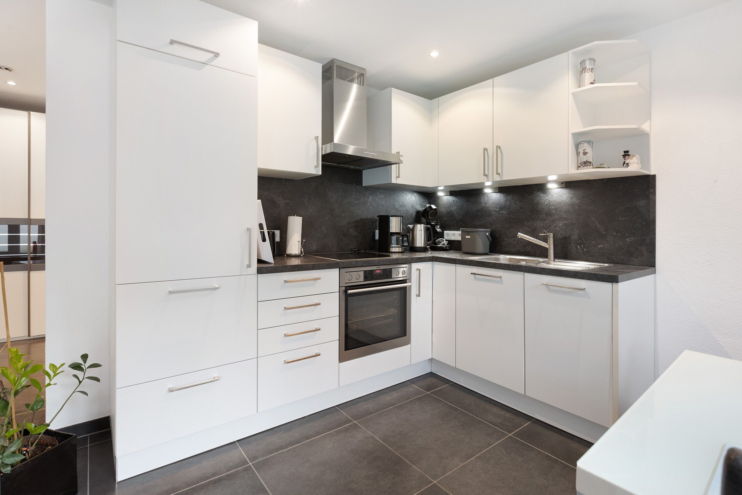 A modern kitchen with white cabinets, a black countertop, stainless steel appliances, and a built-in oven.