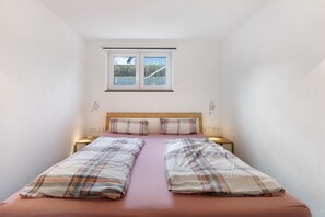 A single bed with plaid bedding, a window with blinds, bedside lamps, and a small table. - Goldbecker Apartment with Private Terrace and Wi-Fi (Gaienhofen)