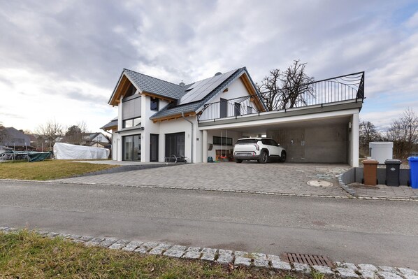 A modern two-story house with a garage, a covered driveway, and a white car parked inside. - Goldbecker Apartment with Private Terrace and Wi-Fi (Gaienhofen)