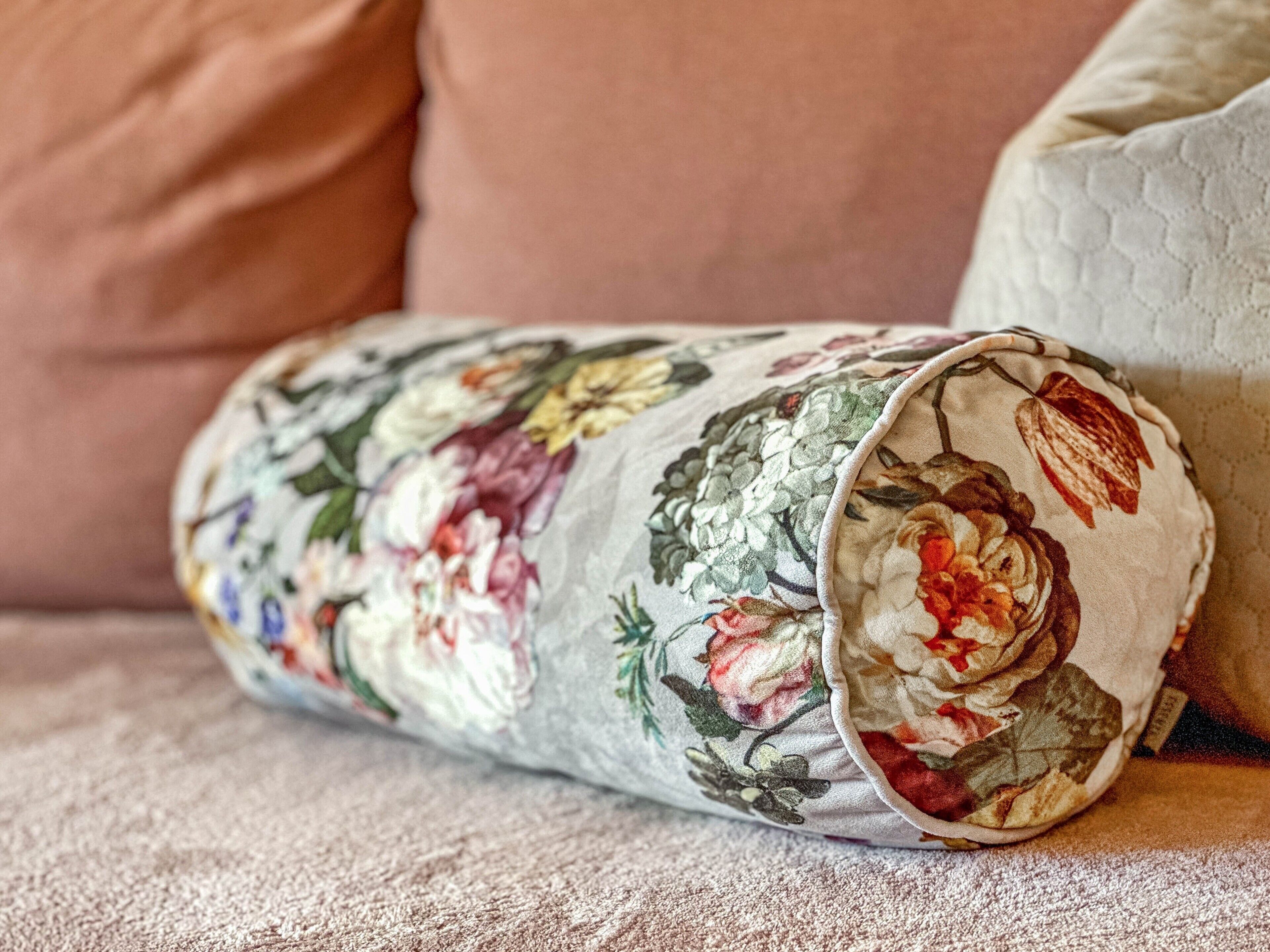 Un coussin à motifs floraux enroulé, posé sur une surface en tissu texturé.