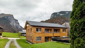 A two-story wooden house with a gravel driveway, surrounded by a green lawn and mountains in the background. - Design Apartment Au with Mountain View, Balcony and Wi-Fi (Au)