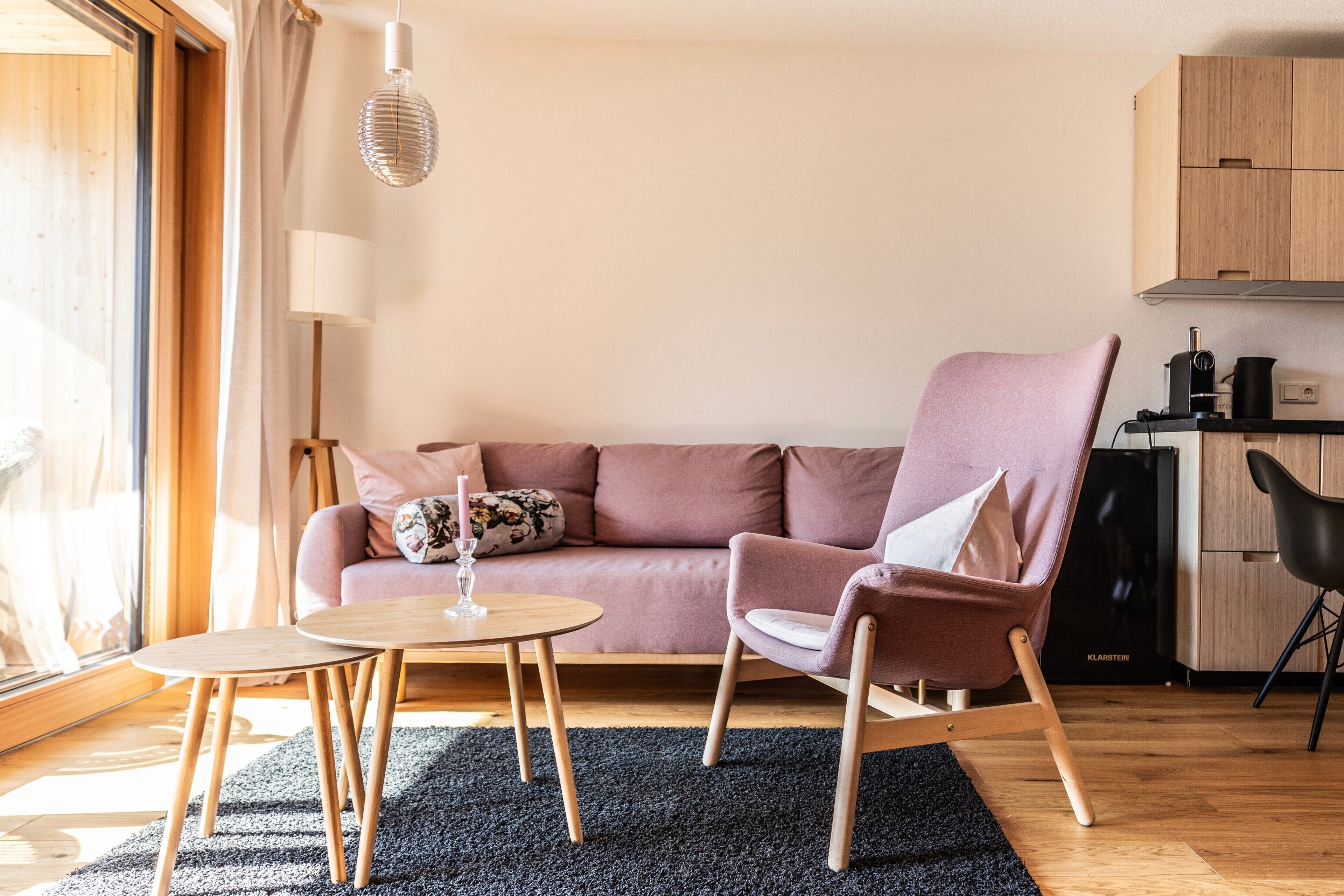 En moderne stue med en sofa, en lænestol, et lille bord og et køkken i baggrunden.