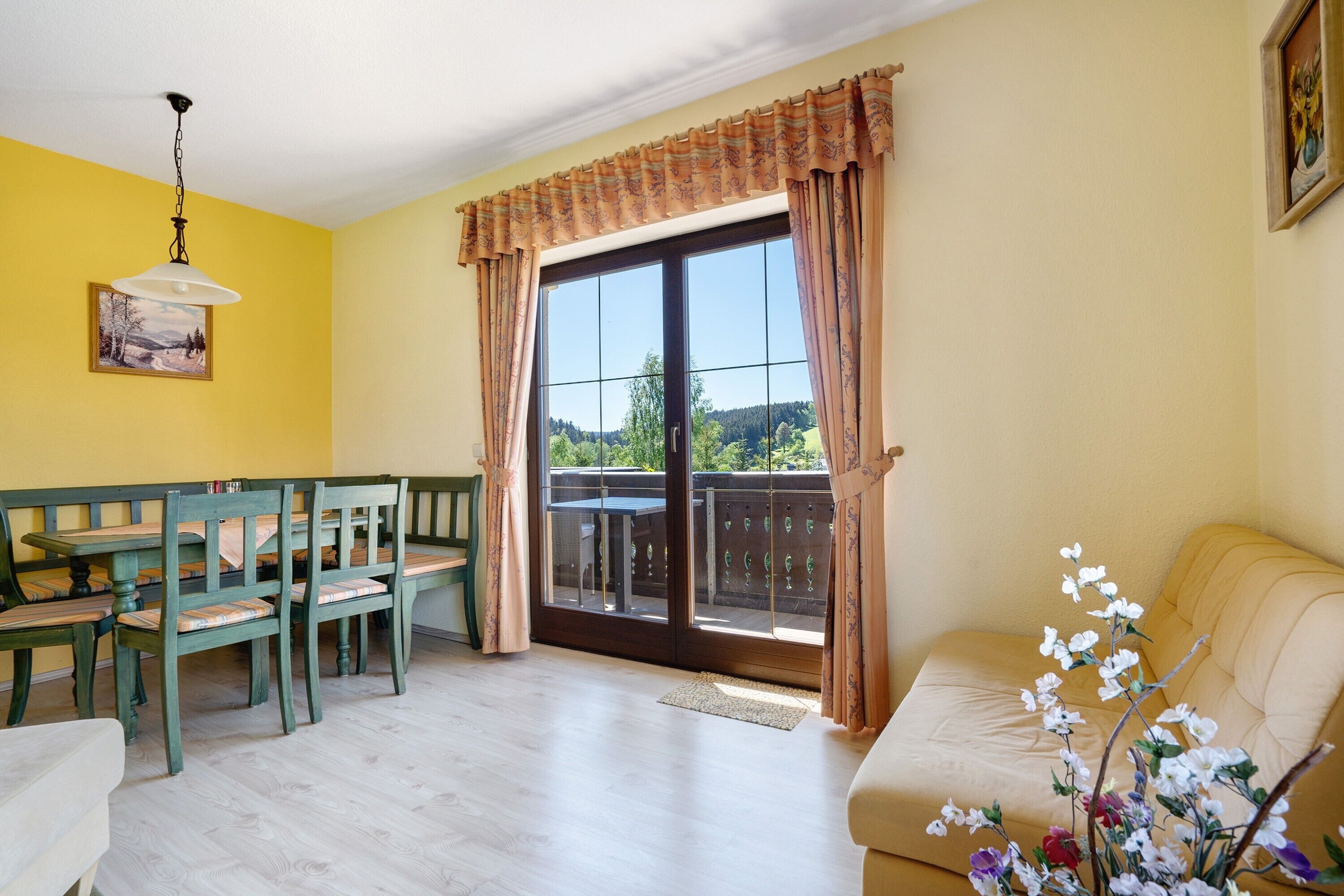 Une pièce comprenant une table à manger et des chaises, un canapé, une fenêtre avec des rideaux et un tableau accroché au mur.