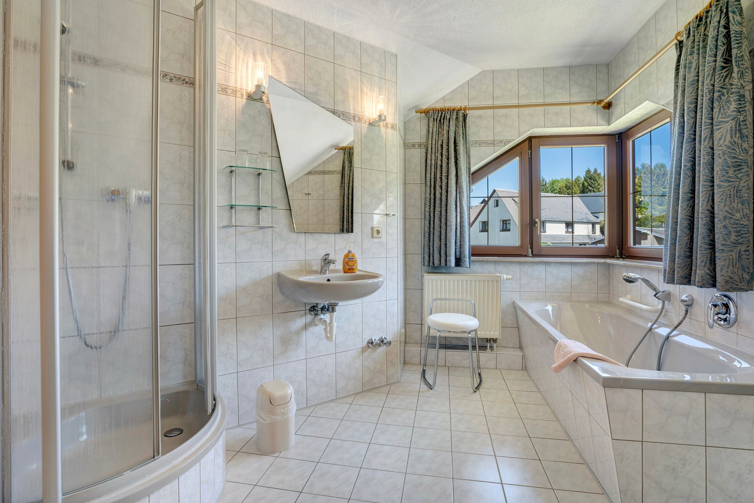 Ein Badezimmer mit Dusche, Waschbecken und Badewanne, großen Fenstern und Blick auf Häuser.