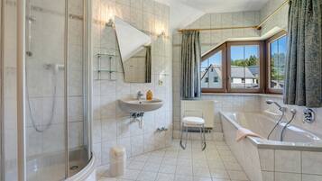 Ein Badezimmer mit Dusche, Waschbecken und Badewanne, großen Fenstern und Blick auf Häuser.