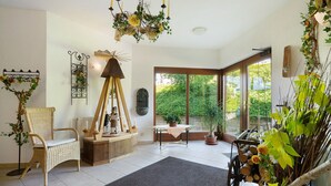 A room with a large window, a wicker chair, a wooden table, and a chandelier. - Studio Apartment 'Pension Bergblick - Silberstraße' with Mountain View, Balcony and Wi-Fi (Marienberg)