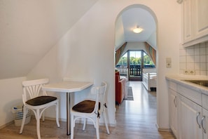 A dining area with two white chairs, a small table, and a view of a balcony with a railing.
