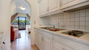 A kitchen with white cabinets, a sink, and a stove. There is a view through an archway to a balcony with a railing. - Studio Apartment 'Pension Bergblick - Silberstraße' with Mountain View, Balcony and Wi-Fi (Marienberg)