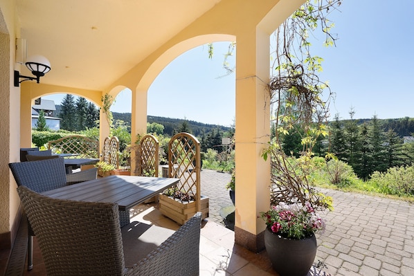 An outdoor patio with wicker furniture, a wooden table, and a potted plant.
