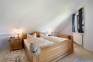 A bedroom with a wooden bed, two bedside tables, a nightstand, a lamp, a radiator, and a window with curtains.