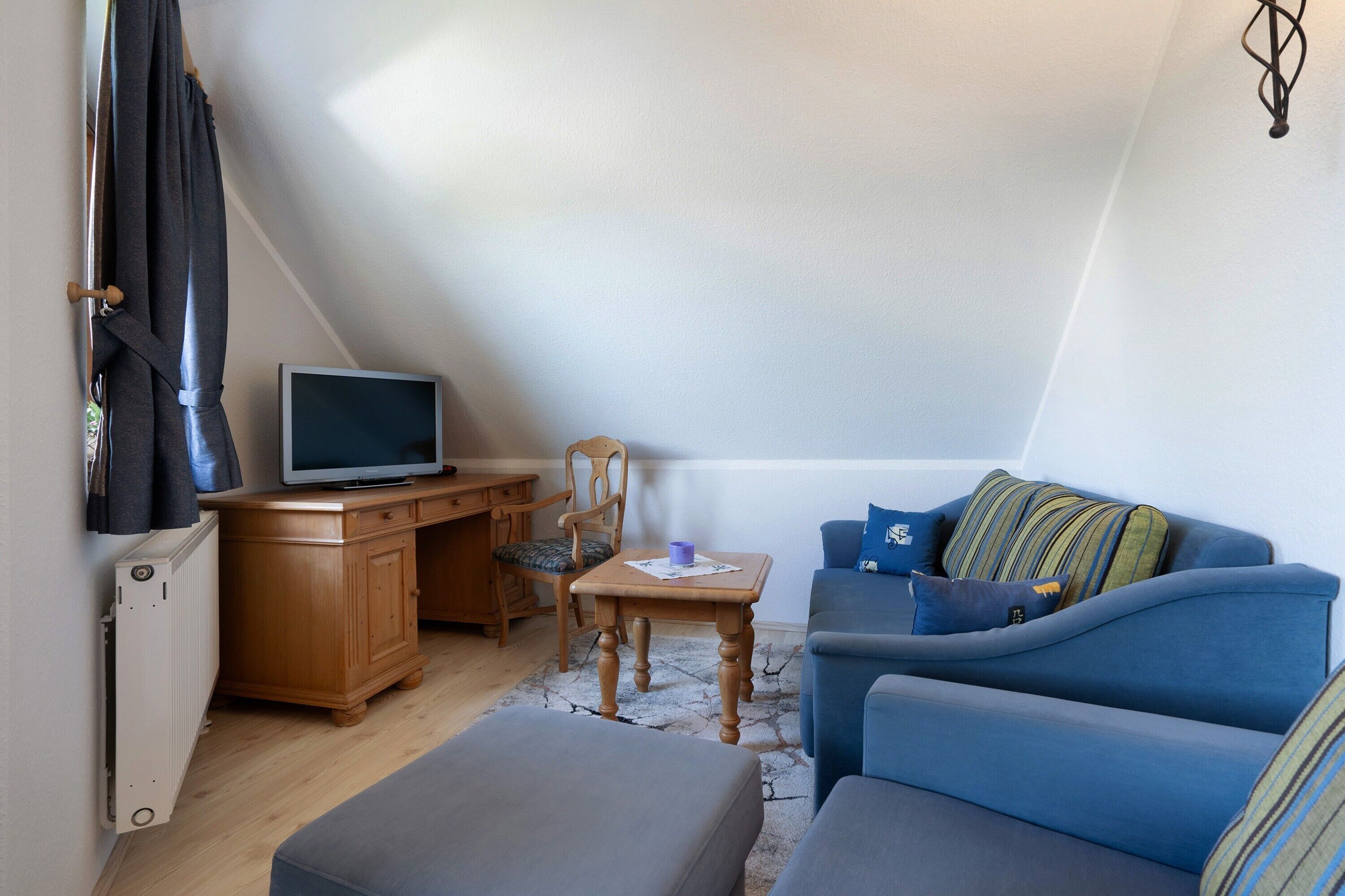 A cozy attic bedroom with a bed, a desk, a chair, a television, and a blue sofa.