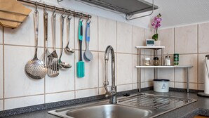 A kitchen with a stainless steel sink, hanging utensils, a clock, and a shelf with kitchen items. - Apartment 'Ferienwohnung Auf Der Insel Rügen' with Shared Terrace and Shared Garden (Bergen auf Rügen)