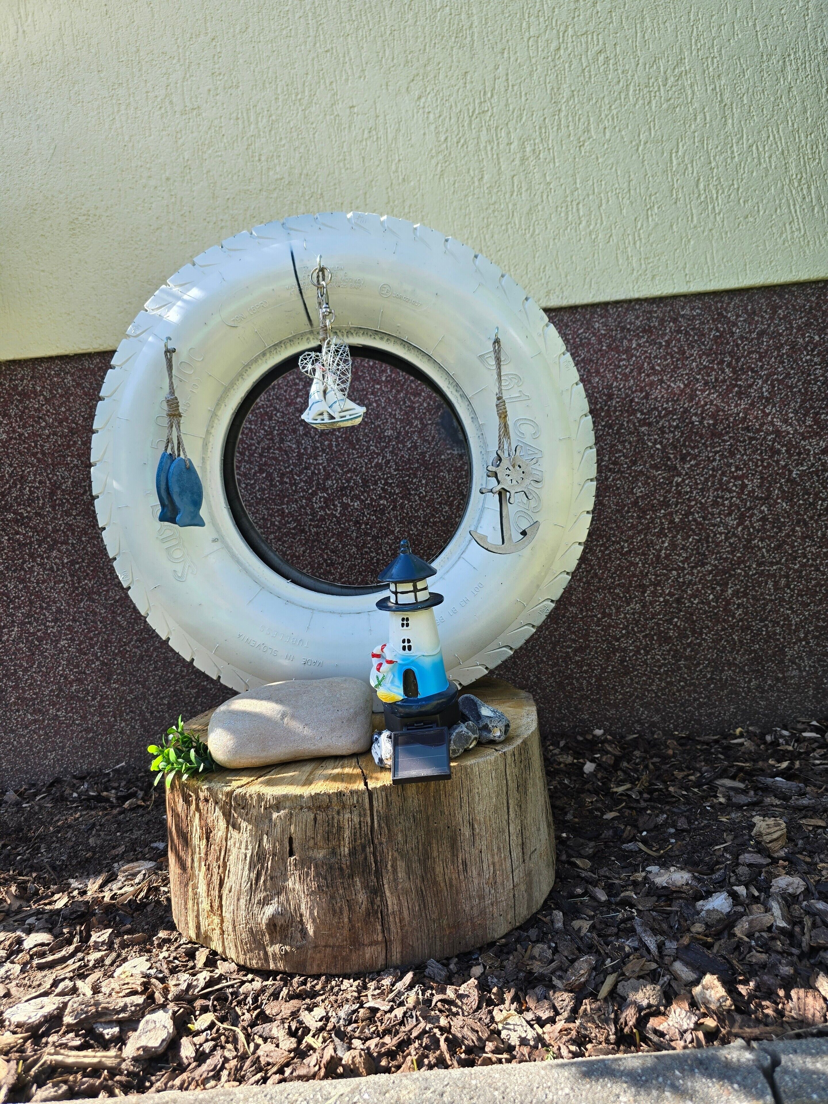Une composition décorative comprenant une maquette de phare posée sur un tronc d'arbre, entourée d'un pneu et de divers petits objets.