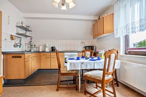 A kitchen with wooden cabinets, a dining table with chairs, a stove, and a window with a view. - Apartment 'Ferienwohnung Auf Der Insel Rügen' with Shared Terrace and Shared Garden (Bergen auf Rügen)
