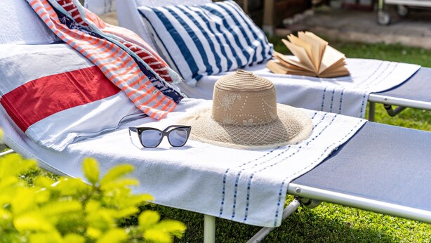 A sun lounger with a striped pillow, a hat, and sunglasses on a table. - Apartment 'Ferienwohnung Auf Der Insel Rügen' with Shared Terrace and Shared Garden (Bergen auf Rügen)