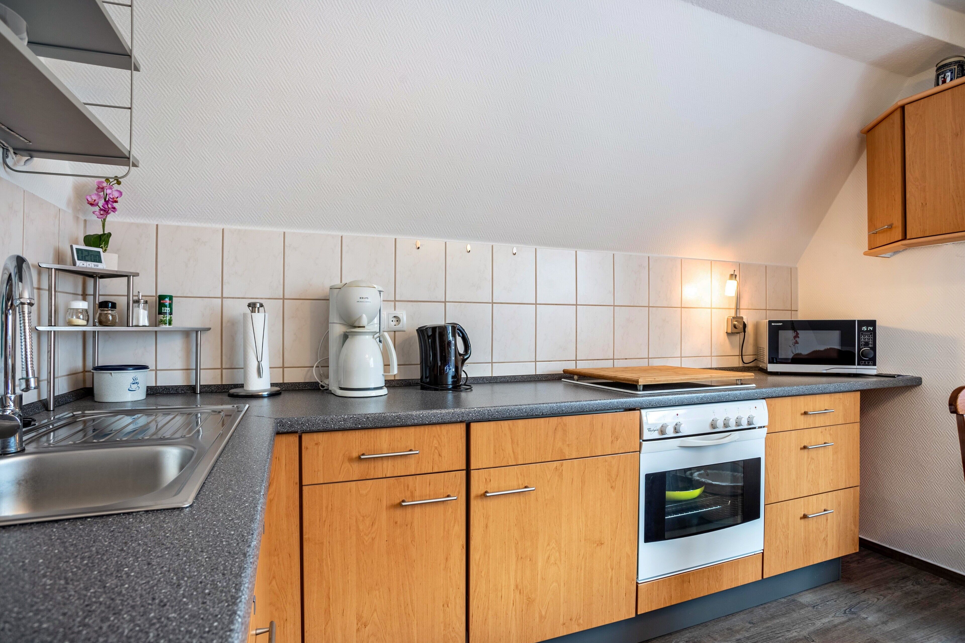 A modern kitchen with a sink, stove, microwave, and wooden cabinets.