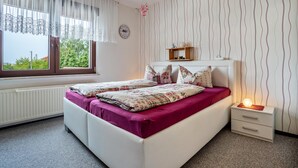 A bedroom with a bed, a bedside table with a lamp, a window with curtains, and a wall with a wavy pattern. - Apartment 'Ferienwohnung Auf Der Insel Rügen' with Shared Terrace and Shared Garden (Bergen auf Rügen)