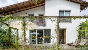 A modern house with a white exterior, wooden roof, and a covered patio with outdoor furniture. - Apartment 'Schambachhof' (Bötzingen am Kaiserstuhl)