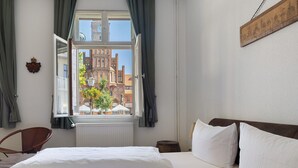Hotelkamer met een bed, een stoel, een raam met gordijnen, een radiator en een aan de muur hangend schilderij.