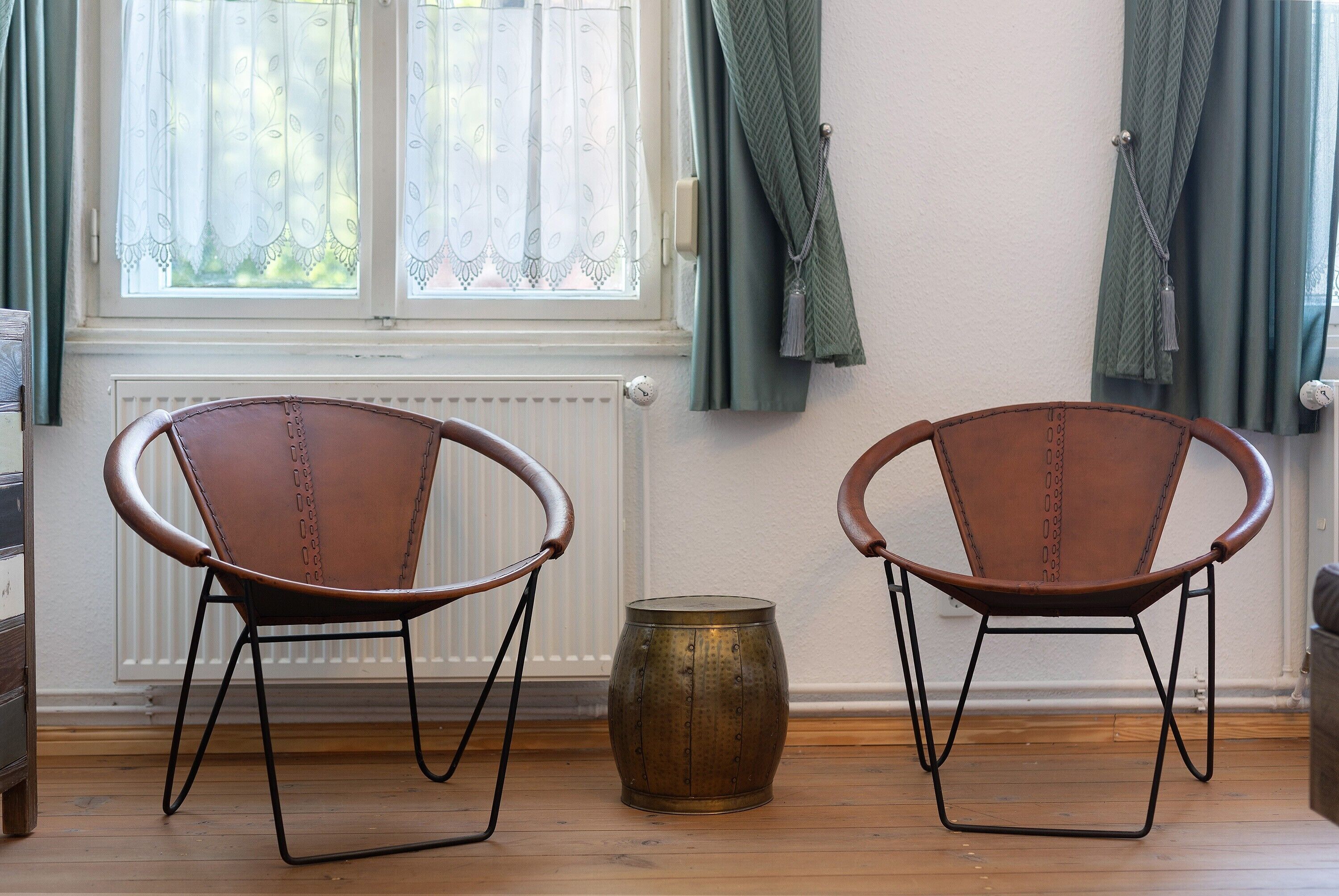 Two leather chairs with metal frames, a brass barrel, and a window with sheer curtains.