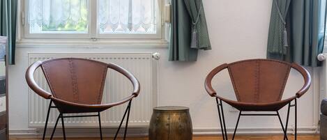 Two leather chairs with metal frames, a brass barrel, and a window with sheer curtains.