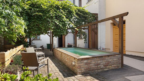 Een zwembadgedeelte met een houten pergola, een betegeld zwembad en buitenmeubels.