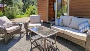 An outdoor seating area with wicker furniture, a glass table, and a sofa with cushions. - Woodland Retreat: Cozy Cabin Near Trails & Mazama (Winthrop)