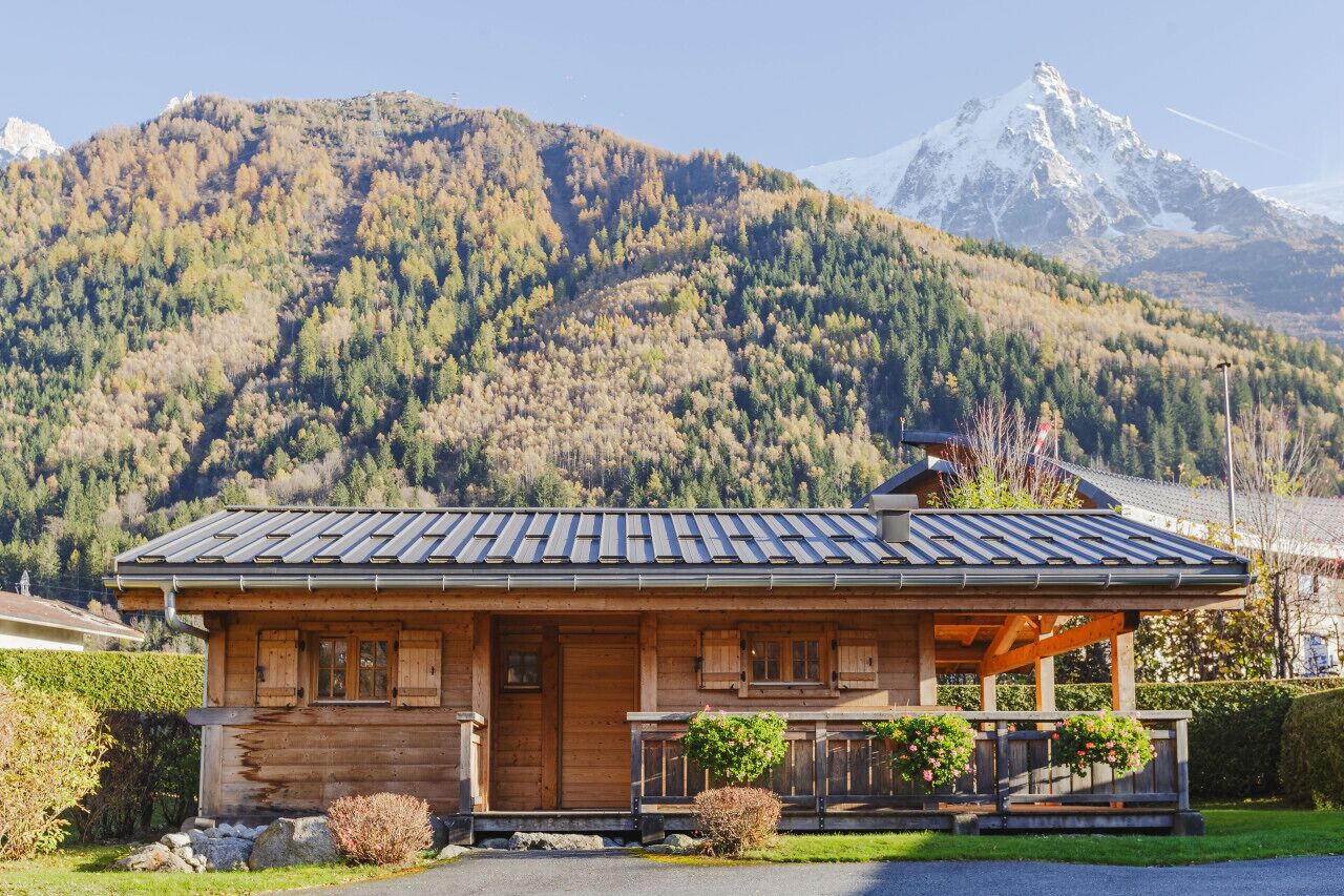 Una baita di legno con tetto spiovente, un portico con ringhiere e vista su una catena montuosa.